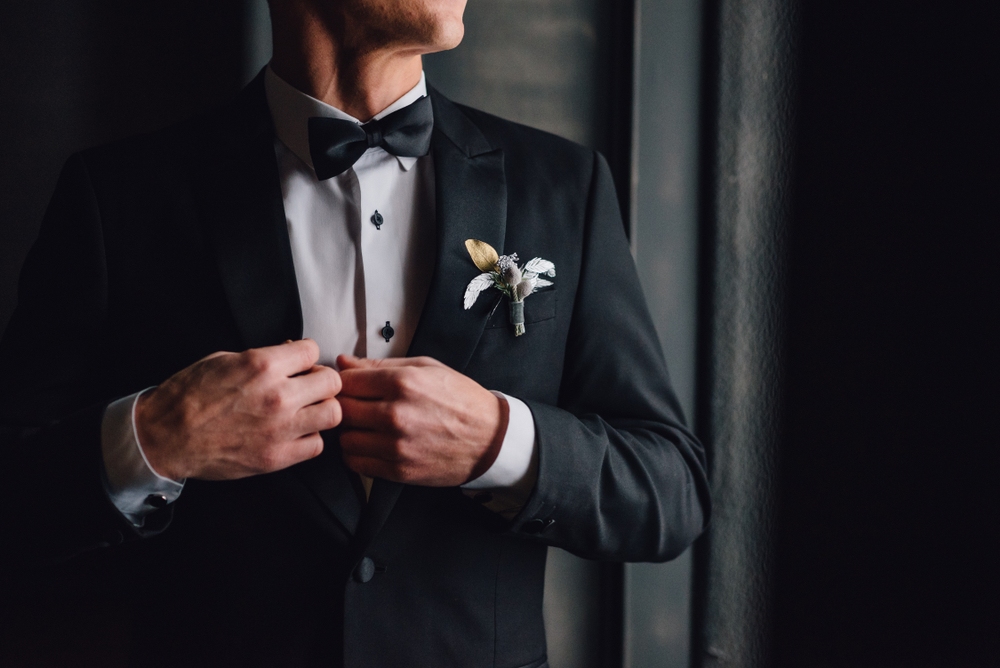 Costume de mariage noir classique, accessoire broche fleurie sobre